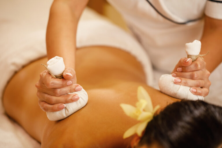 Close-up of woman getting back massage with detox herbal compresses at spa salon.